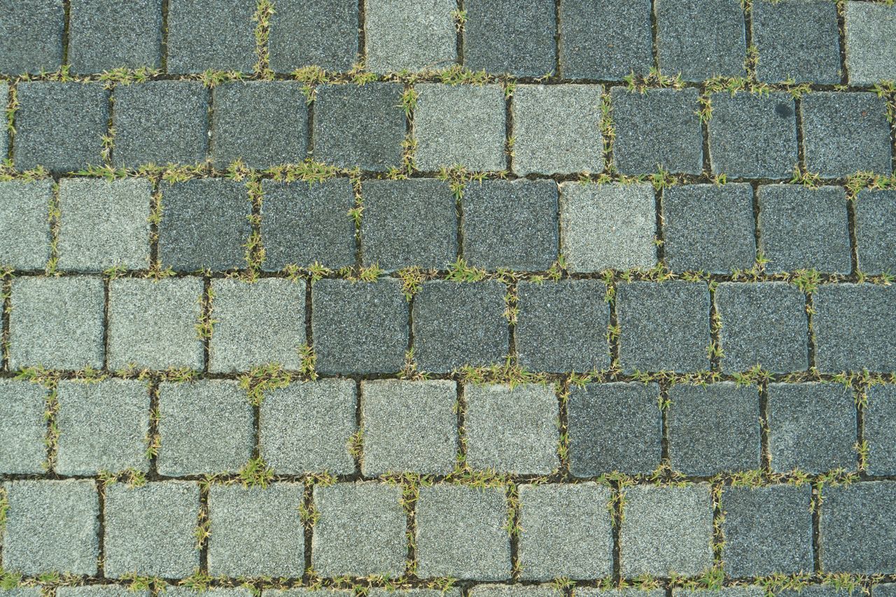 Close-up of a stone paved sidewalk with grass growing between the stones in Toyohashi, Japan.