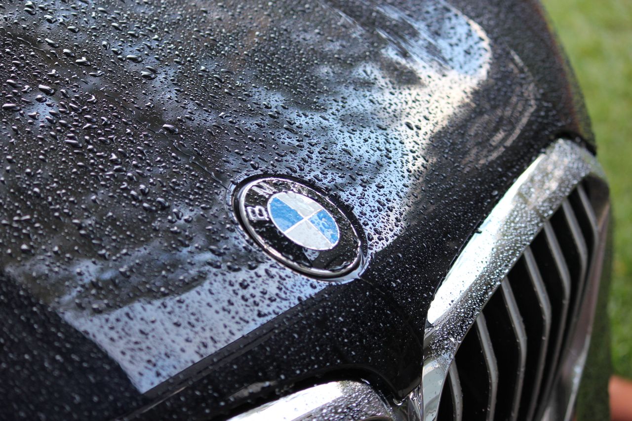 Rain-covered hood of a luxury car featuring a well-known logo.