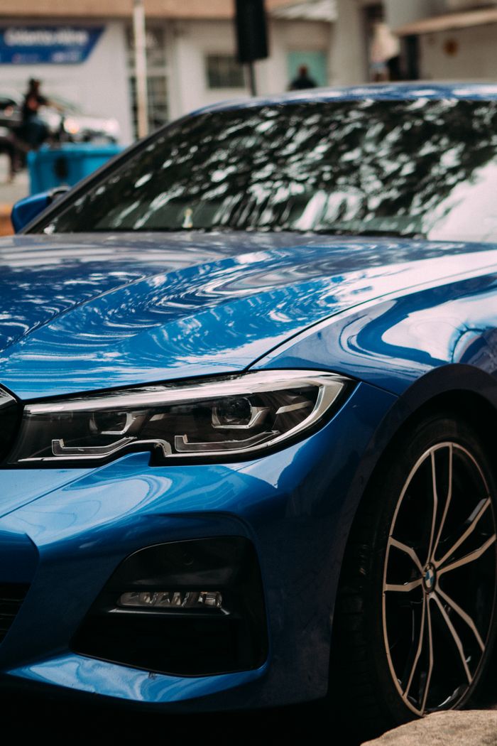 Close-up of a shiny blue car with reflections, parked outdoors on a street.