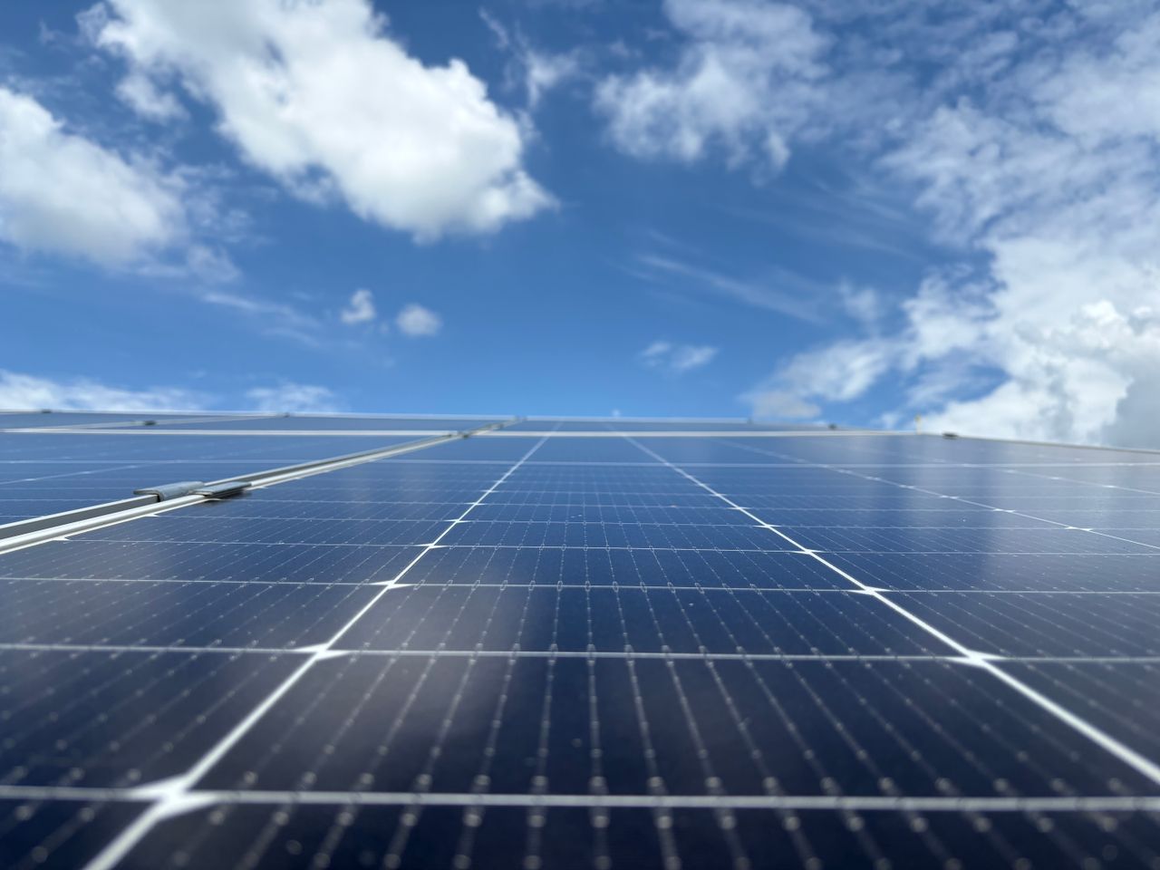 Close-up of solar panels with a clear blue sky and fluffy clouds in Dehradun, India.