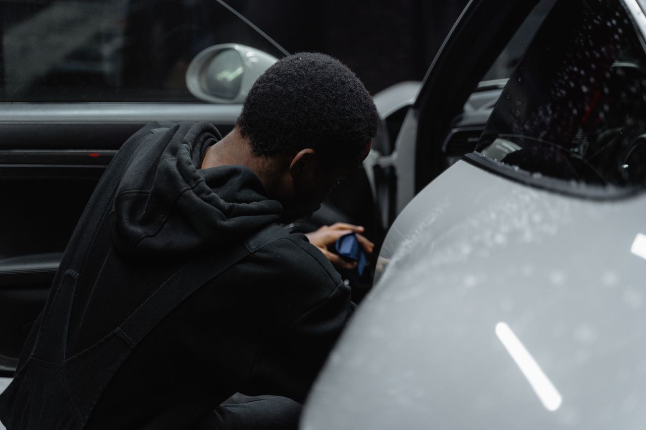 A person is meticulously detailing a luxury car interior under dim lighting, highlighting precision and care.
