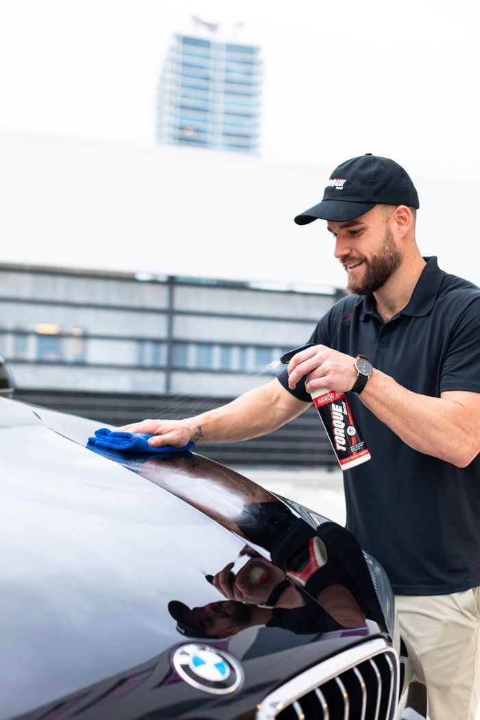 Man polishing a luxury car using a cleaning spray and cloth outdoors.