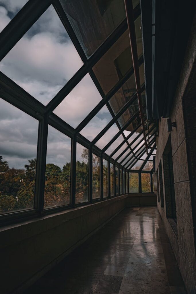 A modern indoor corridor with a glass ceiling, offering a scenic view of the sky and trees.