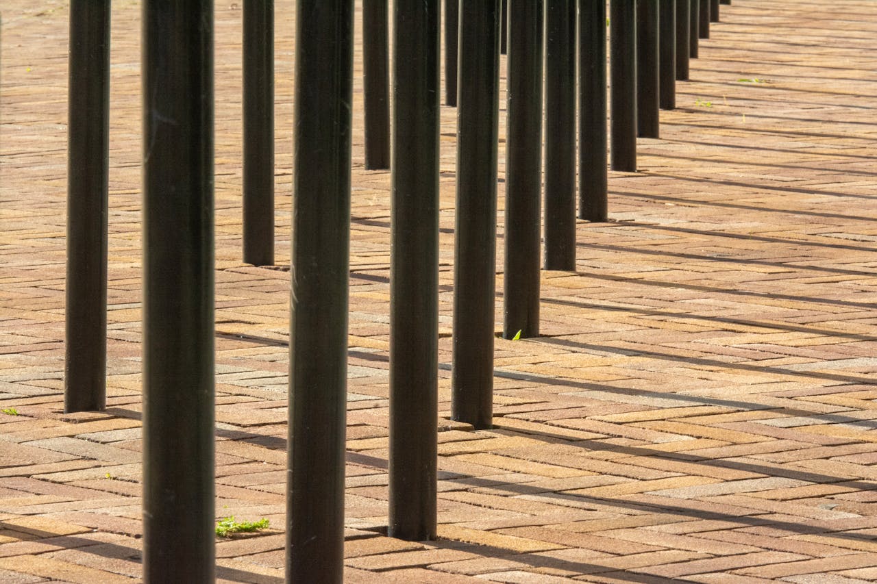 Artistic capture of vertical poles casting shadows on brick pavement.